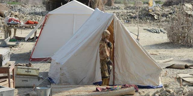 A Pakistani earthquake survivor stands outside her tent near collapsed mud houses in the Dhall Bedi Peerander area of the earthquake-devastated district of Awaran on September 27, 2013