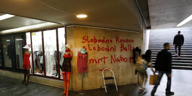 FILE - In this Tuesday April 4, 2017 file photo, people pass through an underground passage with graffiti on the wall that reads: "Free Kosovo, Free Balkan, Death for NATO", in Belgrade, Serbia. The small Adriatic state of Montenegro is set to formally approve becoming a member of NATO, a historic step for the Balkan country that has been split in loyalties to the West and traditional ally Russia. (AP Photo/Darko Vojinovic, File)