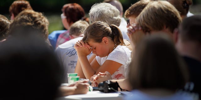 CANNON FALLS, MN - AUGUST 15: People waiting for the arrival of U.S. pray together before the town hall style meeting at the Lower Hannah's Bend Park on August 15, 2011 in Cannon Falls, Minnesota. Obama is on a bus tour of Minnesota, Iowa and Illinois where he is scheduled to speak with people about economic issues at town hall style meetings.  (Photo by Joe Raedle/Getty Images)