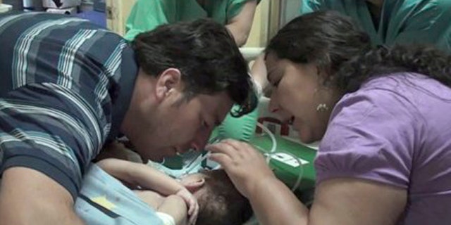 December 13, 2011: In this image taken from a video released by Luis Calvo Mackenna hospital, Jessica Navarrete, right, and Roberto Paredes, parents of conjoined twins Maria Paz and Maria Jose Paredes Navarrete kiss them before a separation surgery in Santiago, Chile.