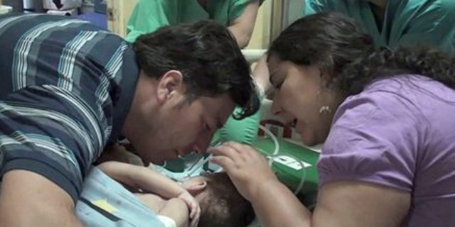 December 13, 2011: In this image taken from a video released by Luis Calvo Mackenna hospital, Jessica Navarrete, right, and Roberto Paredes, parents of conjoined twins Maria Paz and Maria Jose Paredes Navarrete kiss them before a separation surgery in Santiago, Chile.