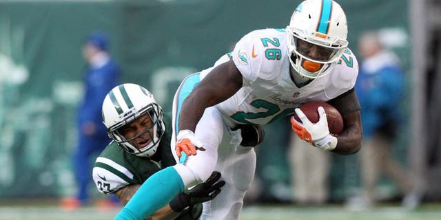Dec 1, 2013; East Rutherford, NJ, USA; Miami Dolphins running back Lamar Miller (26) breaks a tackle by New York Jets corner back Dee Milliner (27) during the third quarter of a game at MetLife Stadium. The Dolphins defeated the Jets 23-3. Mandatory Credit: Brad Penner-USA TODAY Sports