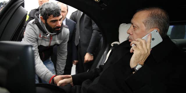 Dec. 25, 2015: Turkish President Recep Tayyip Erdogan, right, takes Vezir Cakras by hand while speaking on his mobile phone inside his car stationed over the Bosporus Bridge in Istanbul.