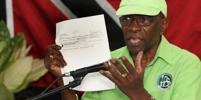 FILE - In this June 3, 2015, file photo, former FIFA vice president Jack Warner hold a copy of a check while he speaks at a political rally in Marabella, Trinidad and Tobago. Trinidad and Tobago’s attorney general has signed documents on Monday, Sept. 21, 2015, that pave the way for U.S. extradition proceedings against Warner. The former FIFA vice president is resisting extradition on U.S. charges of racketeering, wire fraud and money laundering in the FIFA corruption case. (Photo/Anthony Harris, File)