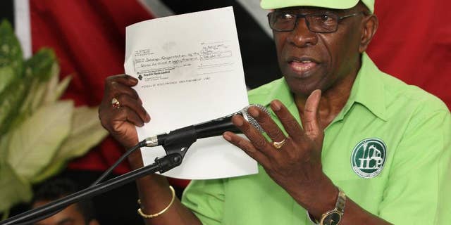 FILE - In this June 3, 2015, file photo, former FIFA vice president Jack Warner hold a copy of a check while he speaks at a political rally in Marabella, Trinidad and Tobago. Trinidad and Tobago’s attorney general has signed documents on Monday, Sept. 21, 2015, that pave the way for U.S. extradition proceedings against Warner. The former FIFA vice president is resisting extradition on U.S. charges of racketeering, wire fraud and money laundering in the FIFA corruption case. (Photo/Anthony Harris, File)