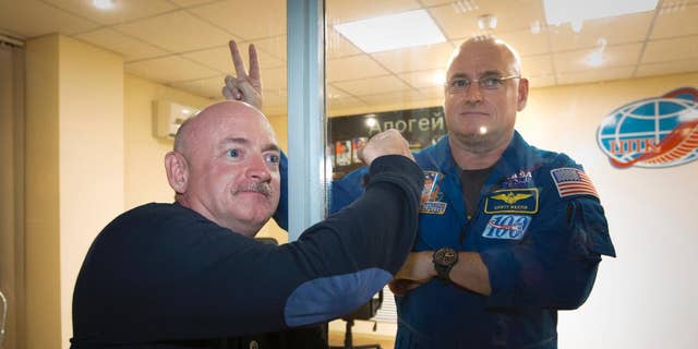 U.S. astronaut Scott Kelly, right, crew member of the mission to the International Space Station, ISS, poses through a safety glass with his brother, Mark Kelly, after a news conference in Russian leased Baikonur cosmodrome, Kazakhstan, Thursday, March 26, 2015.