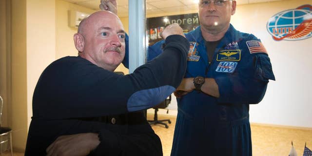 U.S. astronaut Scott Kelly, right, crew member of the mission to the International Space Station, ISS, poses through a safety glass with his brother, Mark Kelly, after a news conference in Russian leased Baikonur cosmodrome, Kazakhstan, Thursday, March 26, 2015.