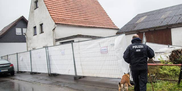 FILE - This is a Tuesday, May 3, 2016 file photo of a police officer with a dog as they pass by a house outside Hoexter, western Germany. German police say they have identified at least four women who survived abuse in the home of a couple suspected of killing two other women. Police said Monday May 9, 2016 that they have contacted the survivors, including a woman from the Berlin area who told investigators she was imprisoned for about three months in the house near the western town of Hoexter. (Marcel Kusch/dpa via AP) GERMANY OUT AUSTRIA OUT SWITZERLAND OUT