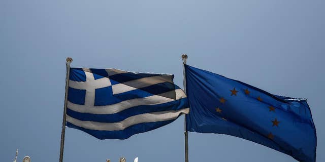 A Greek and a European Union flags flutter in front of statues of goddess Athena, left, and Nautilia, in front of Benaki museum in Athens, Greece, on Wednesday, June 17, 2015. Athens must pay 1.6 billion euros ($1.8 billion) off its debts at the end of the month to avoid a possible default and secure its cherished place among the 19 countries using the single currency.(AP Photo/Yorgos Karahalis)