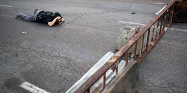 A photographer takes pictures of barricades set up by anti-government protesters in the Altamira neighborhood of Caracas, Venezuela, Thursday, Feb. 20, 2014. Violence is heating up in Venezuela as an opposition leader faces criminal charges for organizing a rally that set off escalating turmoil in the oil-rich, but economically struggling country. (AP Photo/Rodrigo Abd)