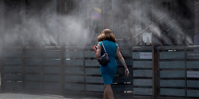 A woman walks along a row of misters Monday, June 19, 2017 in Tempe, Ariz. The forecast calls for a high of 118 on Monday and 120 on Tuesday in Phoenix. (AP Photo/Matt York)