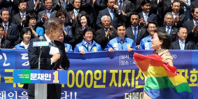 A protester holding a rainbow flag, approaches South Korea's presidential candidate Moon Jae-in from the Democratic Party, left, at National Assembly in Seoul, South Korea, Wednesday, April 26, 2017. South Korean presidential front-runner Moon Jae-in has outraged persecuted sexual minority groups by saying during a television debate that he opposes homosexuality. (Ahn Jung-won/Yonhap via AP)