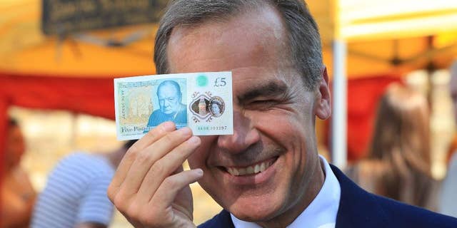 Bank of England Governor Mark Carney holds a new plastic £5 note as he visits Whitecross Street market in London, Tuesday, Sept. 13, 2016. The polymer note is said by the Bank of England to be cleaner, safer and stronger than paper notes, lasting around five years longer. (Jonathan Brady/PA via AP)