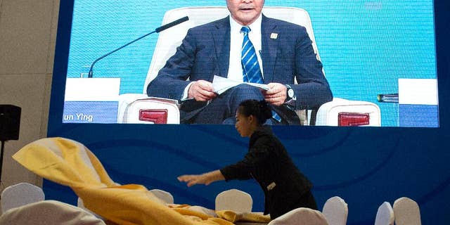 A Chinese waitress lays out a table cloth as Hong Kong's Chief Executive Leung Chun-ying appears on a live broadcast at a dining area of the media center for the Asia-Pacific Economic Cooperation (APEC) Economic meetings held in Beijing, China, Sunday, Nov. 9, 2014. (AP Photo/Ng Han Guan)
