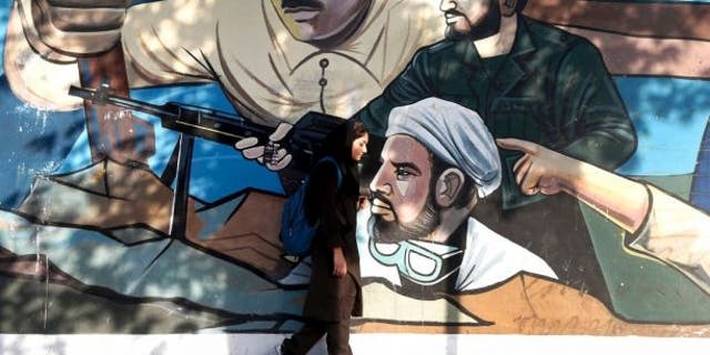 An Iranian woman walks past a mural depicting members of Basij paramilitary force, portraying Iranians' solidarity against their enemies, painted on the wall of a government building at the Felestin (Palestine) Sq. in downtown Tehran