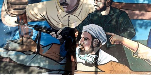 An Iranian woman walks past a mural depicting members of Basij paramilitary force, portraying Iranians' solidarity against their enemies, painted on the wall of a government building at the Felestin (Palestine) Sq. in downtown Tehran