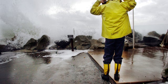 CARDIFF BY THE SEA, CA - DECEMBER 20: Encinitas fireman Mike Kemp adjusts his hood as a wave crashes over a sea wall December 20, 2002 in Cardiff By the Sea, California. Heavy rains and large surf pounded the West Coast as a product of El Nino with the region expecting above average rainfall totals this winter due to El Nino. (Photo by Sandy Huffaker/Getty Images)
