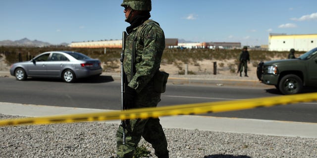 JUAREZ, MEXICO - MARCH 24: A member of the Mexican military police keeps guard over a car, pictured at left, bearing a bullet-ridden body on March 24, 2010 in Juarez, Mexico. Secretary of State Hillary Rodham Clinton, Defense Secretary Robert Gates, and Homeland Security Secretary Janet Napolitano all visited Mexico yesterday for discussions centered on Mexico's endemic drug-related violence. The border city of Juarez, Mexico has been racked by violent drug-related crime recently and has quickly become one of the most dangerous cities in the world in which to live. As drug cartels have been fighting over ever-lucrative drug corridors along the United States border, the murder rate in Juarez has risen to 173 slayings for every 100,000 residents. President Felipe Calderon's strategy of sending 7000 troops to Juarez has not mitigated the situation. With a population of 1.3 million, 2,600 people died in drug-related violence last year and 500 so far this year, including two Americans recently who worked for the U.S. Consulate and were killed as they returned from a child's party. (Photo by Spencer Platt/Getty Images)