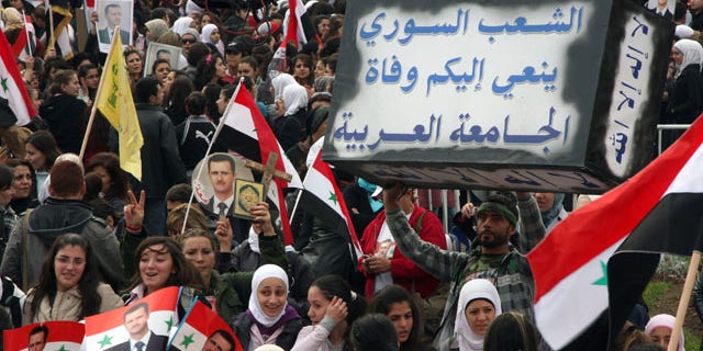 Nov. 24: Pro-Syrian regime protesters shout slogans as one holds a mock coffin with Arabic words reading: 'The Syrian people announce to you the death of the Arab League,' during a protest against the Arab League meeting, in Damascus, Syria.