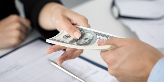 Woman taking batch of hundred dollar bills. Hands close up