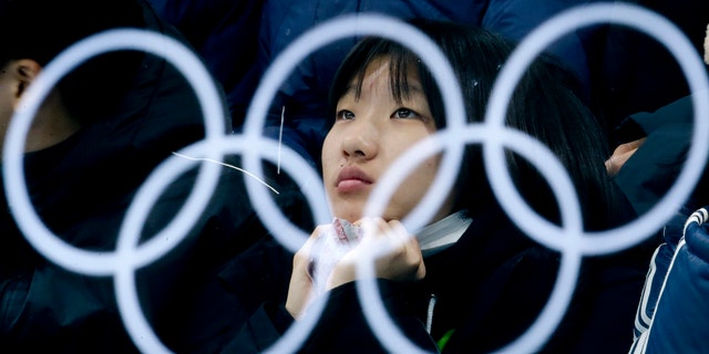 The Olympic rings are reflected in a glass as a spectator watches the mixed doubles semi-final curling match between Canada and Norway at the 2018 Winter Olympics in Gangneung, South Korea, Monday, Feb. 12, 2018. (AP Photo/Natacha Pisarenko)