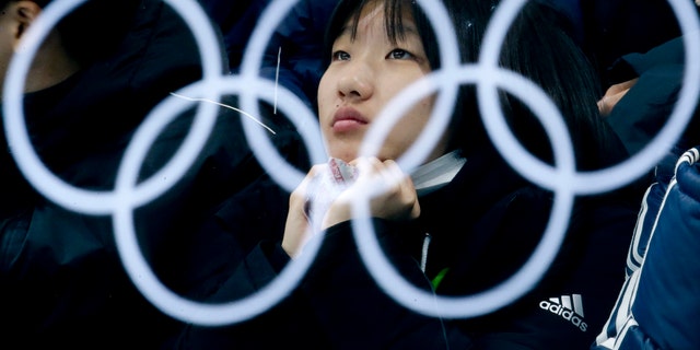 The Olympic rings are reflected in a glass as a spectator watches the mixed doubles semi-final curling match between Canada and Norway at the 2018 Winter Olympics in Gangneung, South Korea, Monday, Feb. 12, 2018. (AP Photo/Natacha Pisarenko)