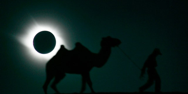 A man and his camel walk past as the sun is blocked by the moon during a solar eclipse in Gaotai, Gansu province August 1, 2008. REUTERS/Aly Song (CHINA) - RTR20JDU