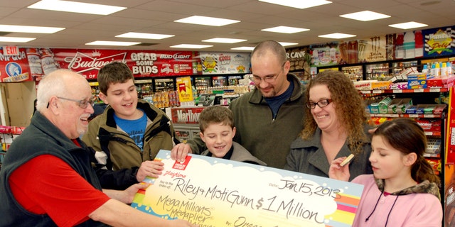 The Gunn family of Wolf Creek, Ore., accepts a symbolic check for $1 million before taxes from Oregon Lottery official Ray Martin on Tuesday, Jan. 15, 2013, at the convenience store where they bought it in Merlin, Ore. Riley Gunn lost his job as a project manager for a telecommunications company in May 2012 and moved his family to a one-room cabin outside Wolf Creek, Ore. While he and his wife were driving home, they pulled off the freeway for corn dogs and pizza pockets and bought an $8 ticket, and won $1 million dollars. Riley and Misti Gunn are at center, with their sons Elijah, 13, left, and Isac, 11, and daughter, Destenie, 9, right. (AP Photo/Jeff Barnard)