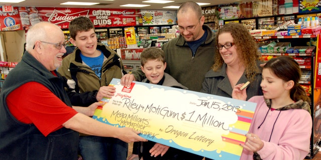 The Gunn family of Wolf Creek, Ore., accepts a symbolic check for $1 million before taxes from Oregon Lottery official Ray Martin on Tuesday, Jan. 15, 2013, at the convenience store where they bought it in Merlin, Ore. Riley Gunn lost his job as a project manager for a telecommunications company in May 2012 and moved his family to a one-room cabin outside Wolf Creek, Ore. While he and his wife were driving home, they pulled off the freeway for corn dogs and pizza pockets and bought an $8 ticket, and won $1 million dollars. Riley and Misti Gunn are at center, with their sons Elijah, 13, left, and Isac, 11, and daughter, Destenie, 9, right. (AP Photo/Jeff Barnard)