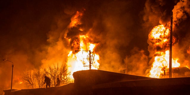 In this photo provided by the Ministry of Emergency Situations Kirov Branch press service, men are silhouetted against burning tankers early Wednesday, Feb. 5, 2014, near Posdino in Kirov region of Russia, some 800 km ( about 500 miles) northeast of Moscow. 32 tankers were derailed and 12 of them burned. No casualties were reported. (AP Photo/ Ministry of Emergency Situations, Kirov Branch Press Service)