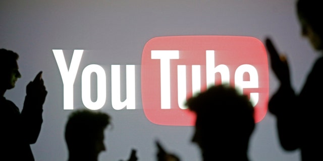 People are silhouetted as they pose with mobile devices in front of a screen projected with a YouTube logo, in this picture illustration taken in Zenica Oct. 29, 2014. (REUTERS/Dado Ruvic)
