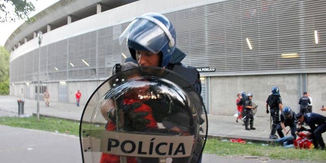 In this May 17 2015 file photo, a riot policeman holds a crying boy as his father is attacked by other policemen with batons, right, outside of a stadium, in Guimaraes, Portugal. Portugal's public prosecutor has filed charges Tuesday April 12, 2016, that could bring a prison sentence of more than 10 years against a policeman who beat a middle-aged football fan in front of his two young sons, with the video of the incident causing a national scandal. (AP Photo/Delfim Machado)