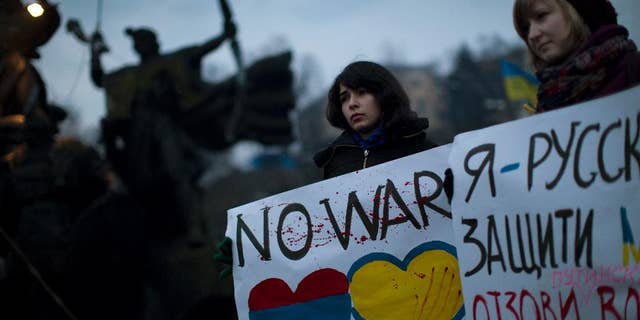 Ukrainian Maria, 23, right, and Vanui, 22, hold posters against Russia's military intervention in Crimea, in Kiev, Ukraine, Sunday, March 2, 2014. Russia's parliament approved a motion to use the country's military in Ukraine after a request from President Vladimir Putin as protests in Russian-speaking cities turned violent Saturday, sparking fears of a wide-scale invasion. The poster in the right side reads in Ukrainian: "I am from Russia, please protect me and remove the weapons and soldiers from Ukraine." (AP Photo/Emilio Morenatti)