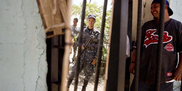 A National Police officer is reflected in a mirror hanging inside the area of gang members from the Mara Salvatrucha, MS, inside the San Pedro Sula prison in Honduras, Tuesday, May 28, 2013. Honduras' largest and most dangerous street gangs have declared a truce, offering the government peace in exchange for rehabilitation and jobs. A Mara Salvatrucha gang spokesman says the gang and its rival, 18th Street, will commit to zero violence and zero crime in the streets as first step show of good faith. (AP Photo/Esteban Felix)