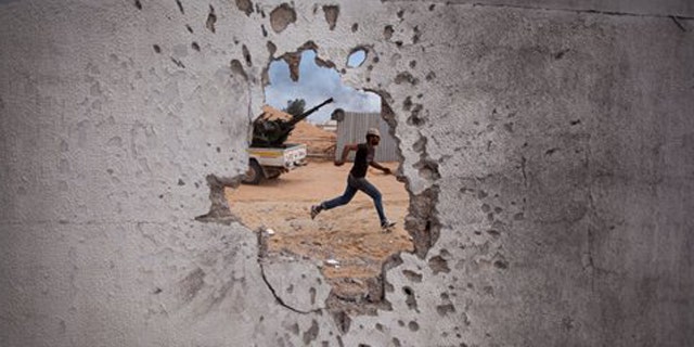 Oct. 7: A Libyan revolutionary fighter runs for cover while attacking pro-Qaddafi forces.