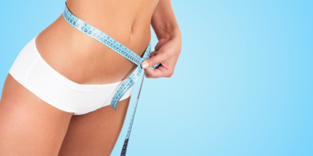 Beautiful woman measuring her waist - high key shot in studio
