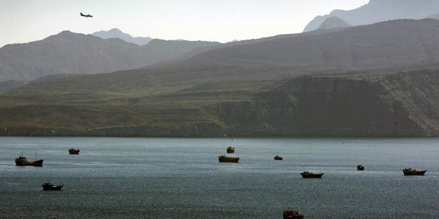 In this Jan. 19, 2012 file photo, a plane flies over the mountains in south of the Strait of Hormuz as the trading dhows and ships are docked on the Persian Gulf waters near the town of Khasab, in Oman.