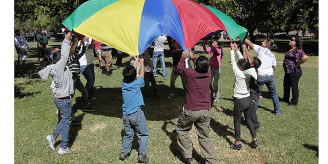 Children and adults uses a play parachute as past of an exercise activity during a wellness program run jointly by the La Familia Counseling Center and the YMCA in Sacramento. The program is funded by 2004's Proposition 63. A fifth of the revenue from the measure goes to activities, like wellness programs. (AP Photo/Rich Pedroncelli)