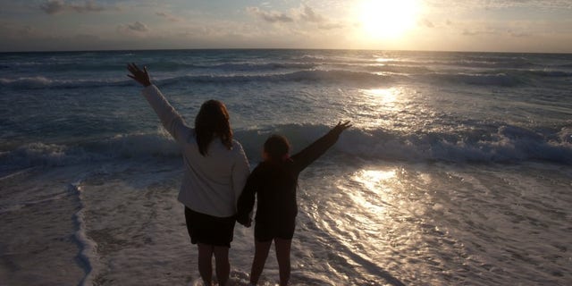 A mother and her daughter raise their hands on a beach at dawn on New Year's Day in Cancun