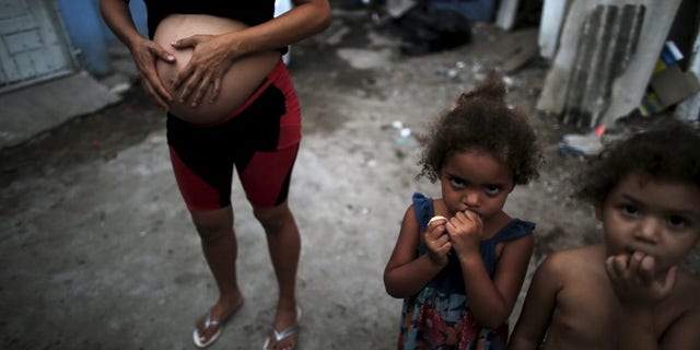 Patricia Araujo, who is seven-months pregnant, stands next to children as they pose in front of their stilt house, a lake dwelling also known as palafitte or 'Palafito', in Recife