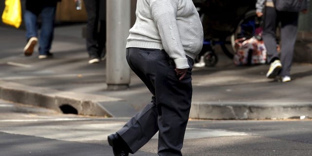 A man crosses a main road as pedestrians carrying food walk along the footpath in central Sydney, Australia