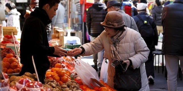 A woman pays money as she buys fruits outside a vegetable store at Ameyoko shopping district in Tokyo