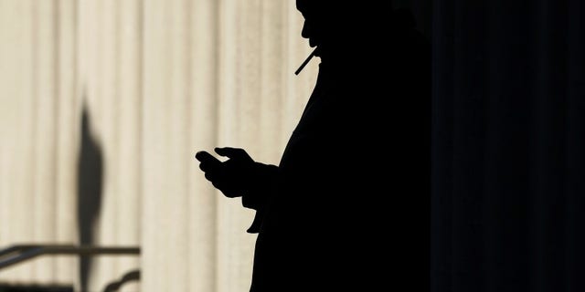A man sends text messages on his mobile phone as he smokes a cigarette outside the court building in San Diego