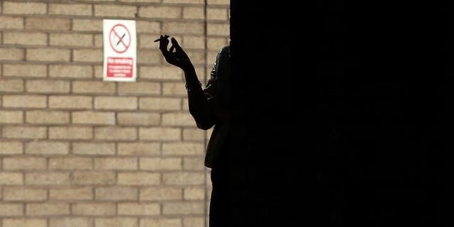 A woman smokes in the shadows outside Southwark Crown Court in central London