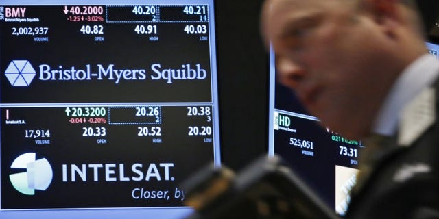 A trader passes by a screen displaying the tickers symbols for Bristol-Myers Squibb and Intelsat, Ltd. on the floor at the New York Stock Exchange