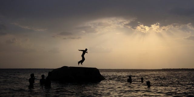 A boy prepares to jump off a rock into the waters of the Osman Sagar Lake near Hyderabad