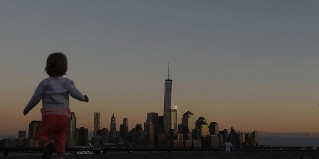 A girl plays in front of the skyline of New York's Lower Manhattan and One World Trade Center in a park along the Hudson River in Hoboken