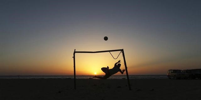A boy jumps to save a goal while playing soccer on the beach in Benghazi
