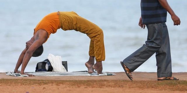 A man performs yoga as another man walks past him at Galle Face Green in Colombo