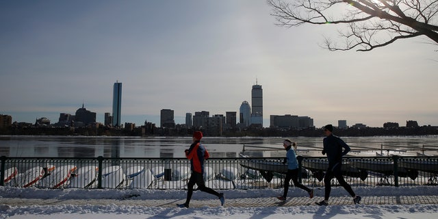 Joggers run along the Charles River past the Boston skyline on a sunny winter's day in Cambridge.